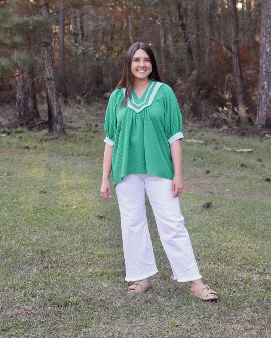 Woman in a green blouse and white pants standing in a forest