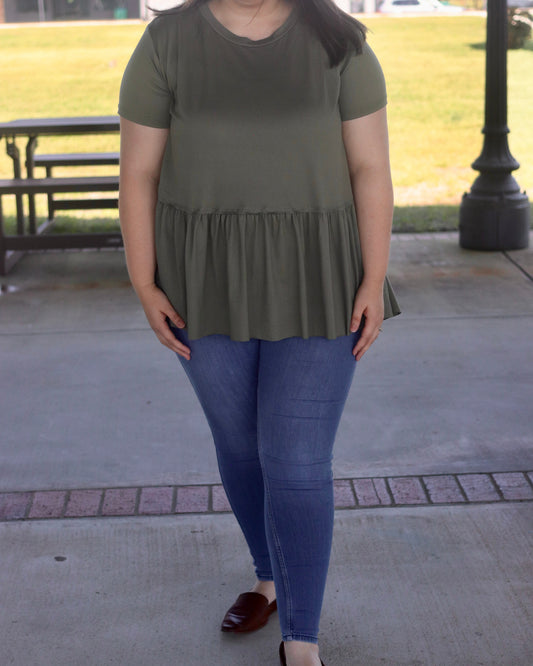 Woman wearing a green tiered dress and blue jeans standing outdoors.