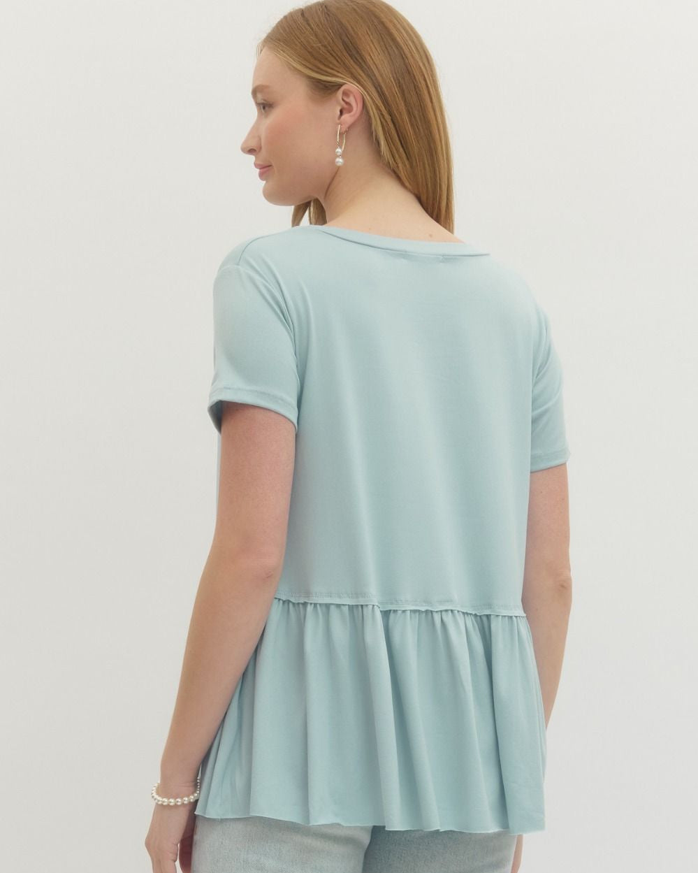 Woman wearing a light blue peplum top and light gray pants on a white background