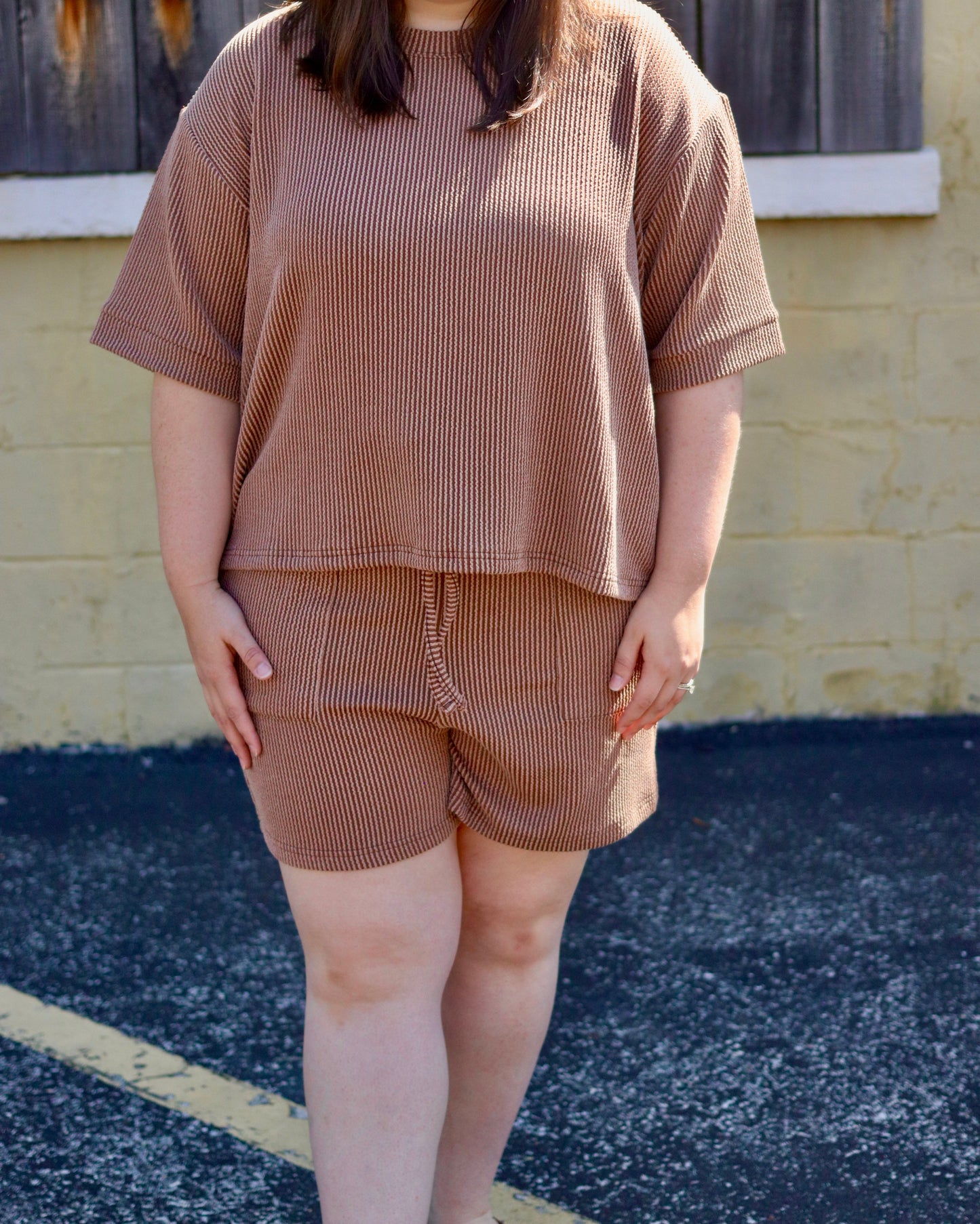 Woman wearing a brown outfit standing in front of a wooden shutter.