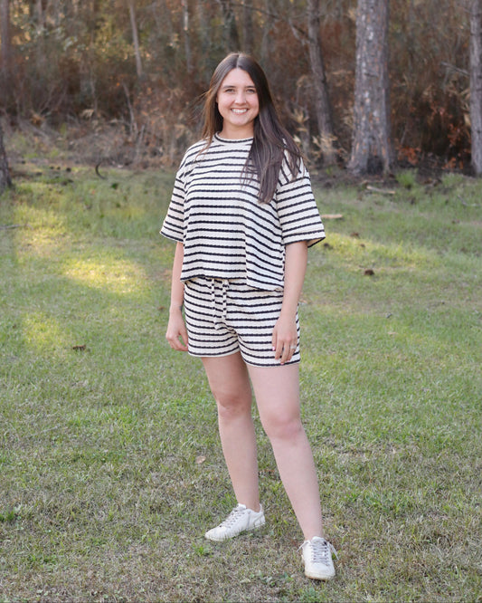 Person wearing a black and white striped outfit standing in a grassy area with trees.