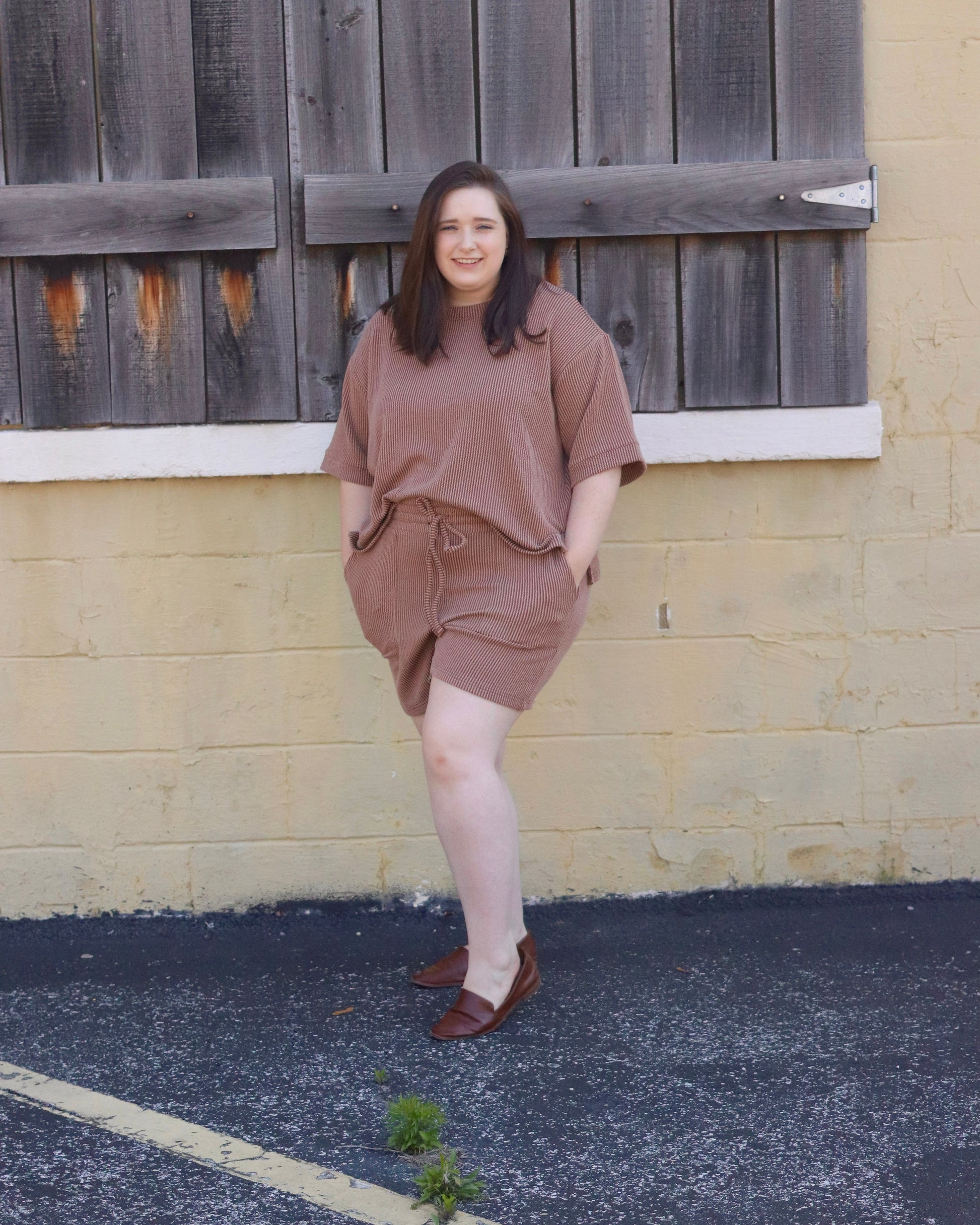 Woman in a brown outfit standing against a textured wall.