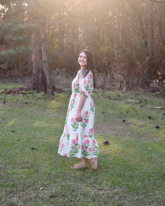 Woman in a floral dress standing in a grassy field with trees in the background