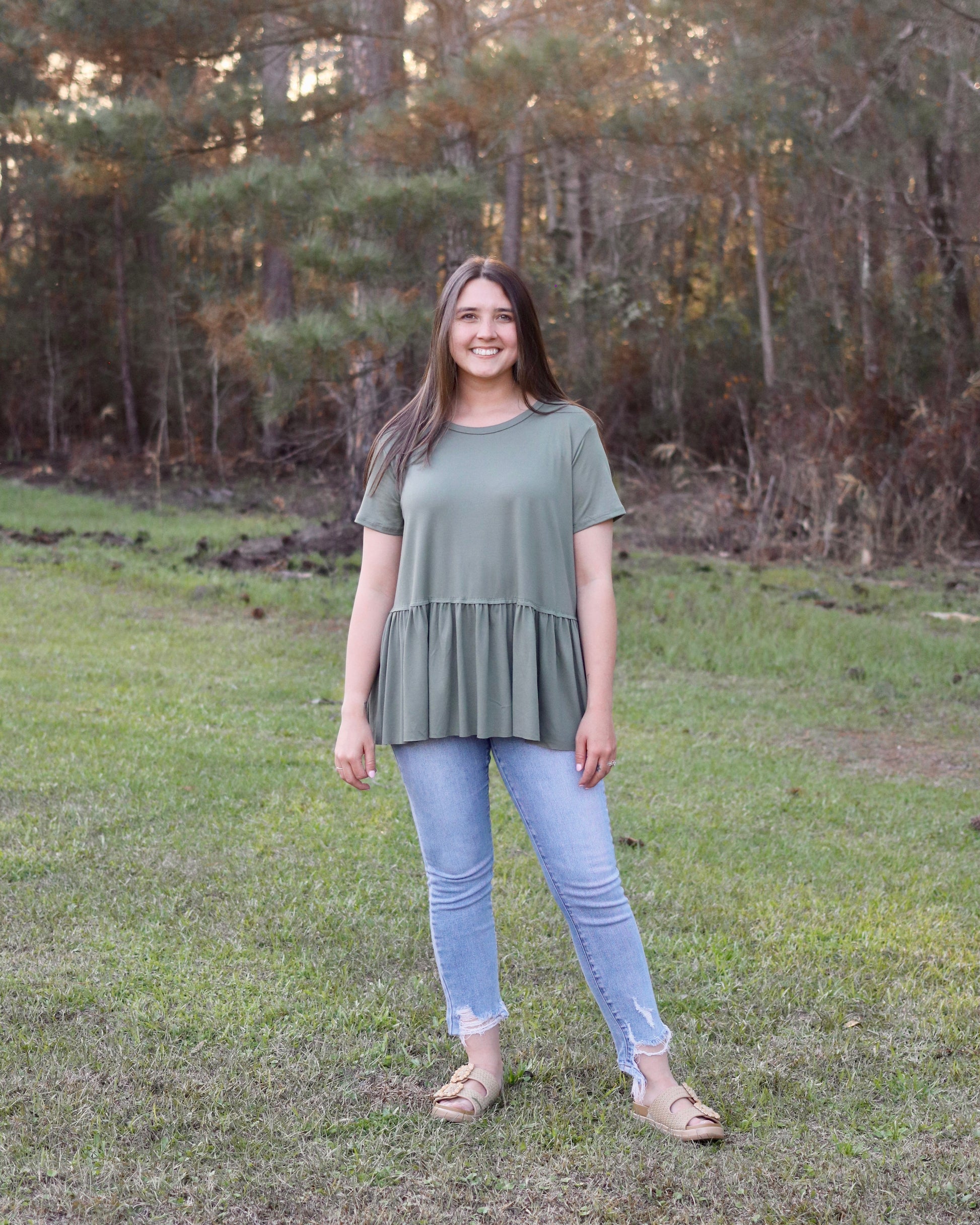 Woman standing in a grassy field with trees in the background