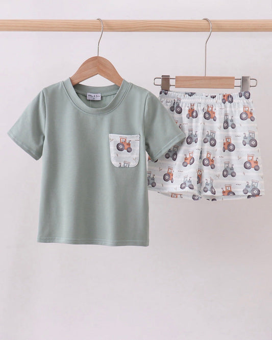 Children's green t-shirt with a pocket design and patterned shorts on a wooden hanger against a white background.