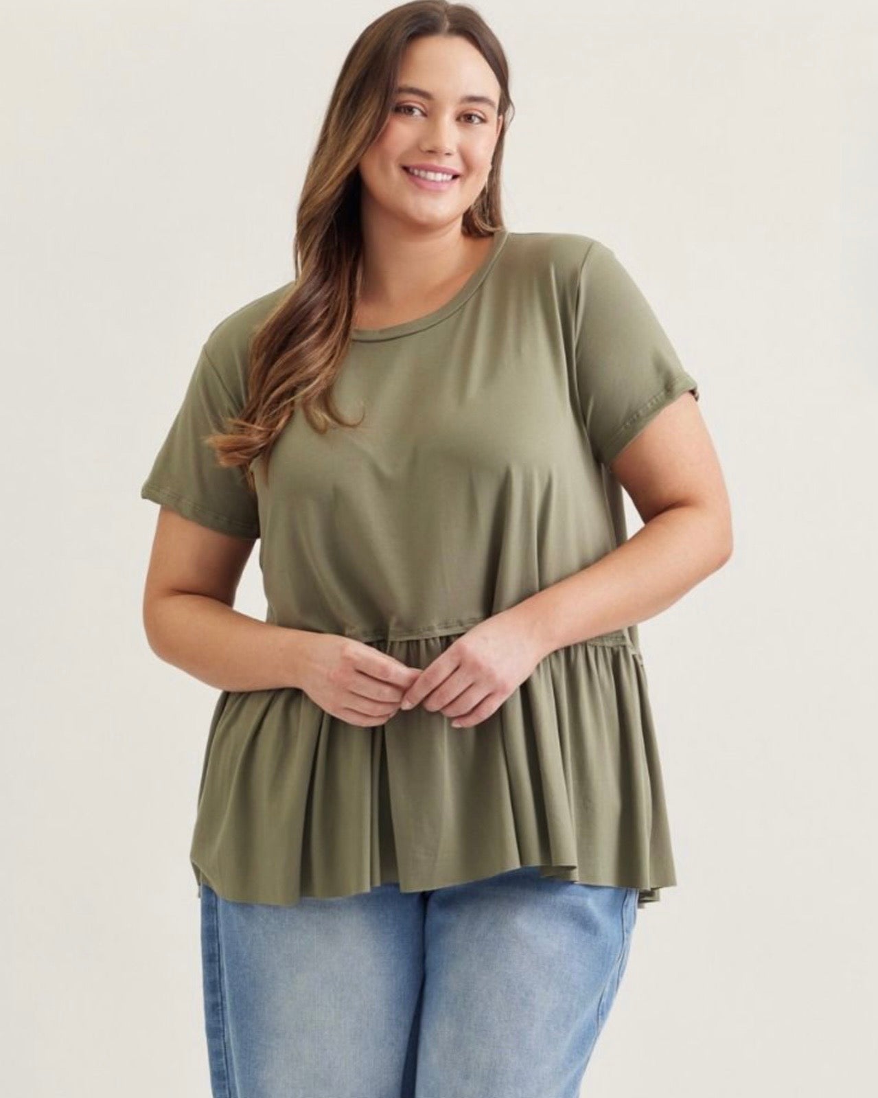 Woman wearing an olive green peplum top and blue jeans on a white background