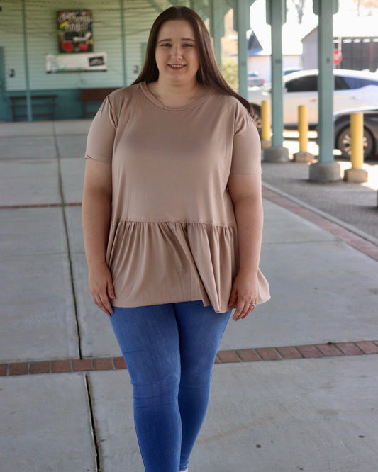 Woman wearing a beige top and blue leggings standing on a sidewalk.