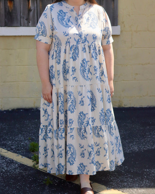 Woman wearing a blue and white floral dress standing in front of a yellow wall.