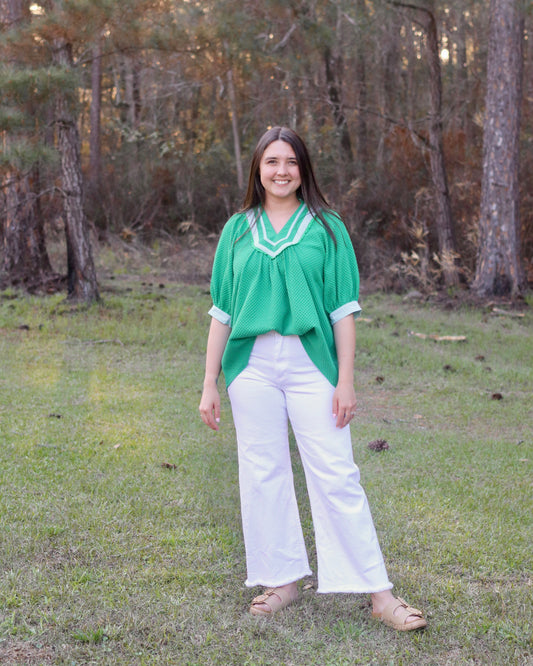Woman in a green top and white pants standing in a forest