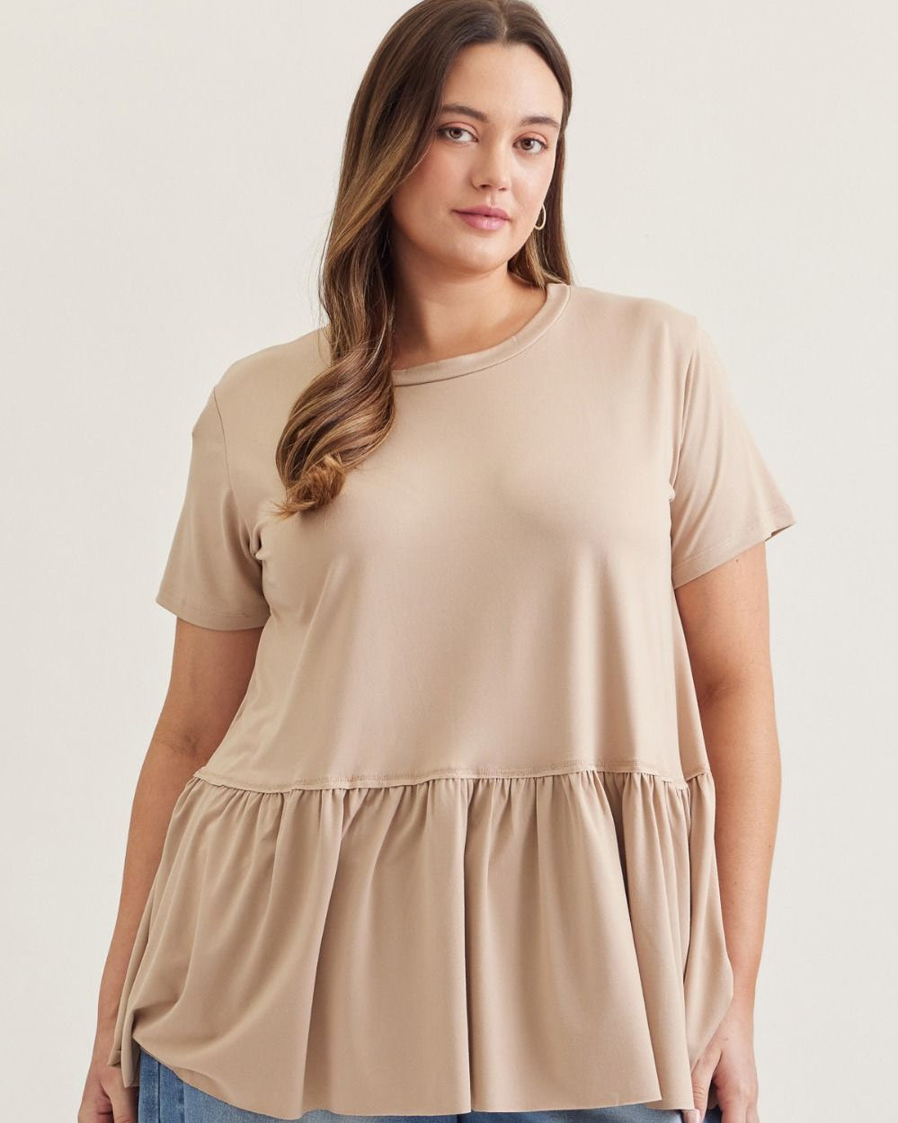 Woman wearing a beige top with a layered skirt design on a plain background
