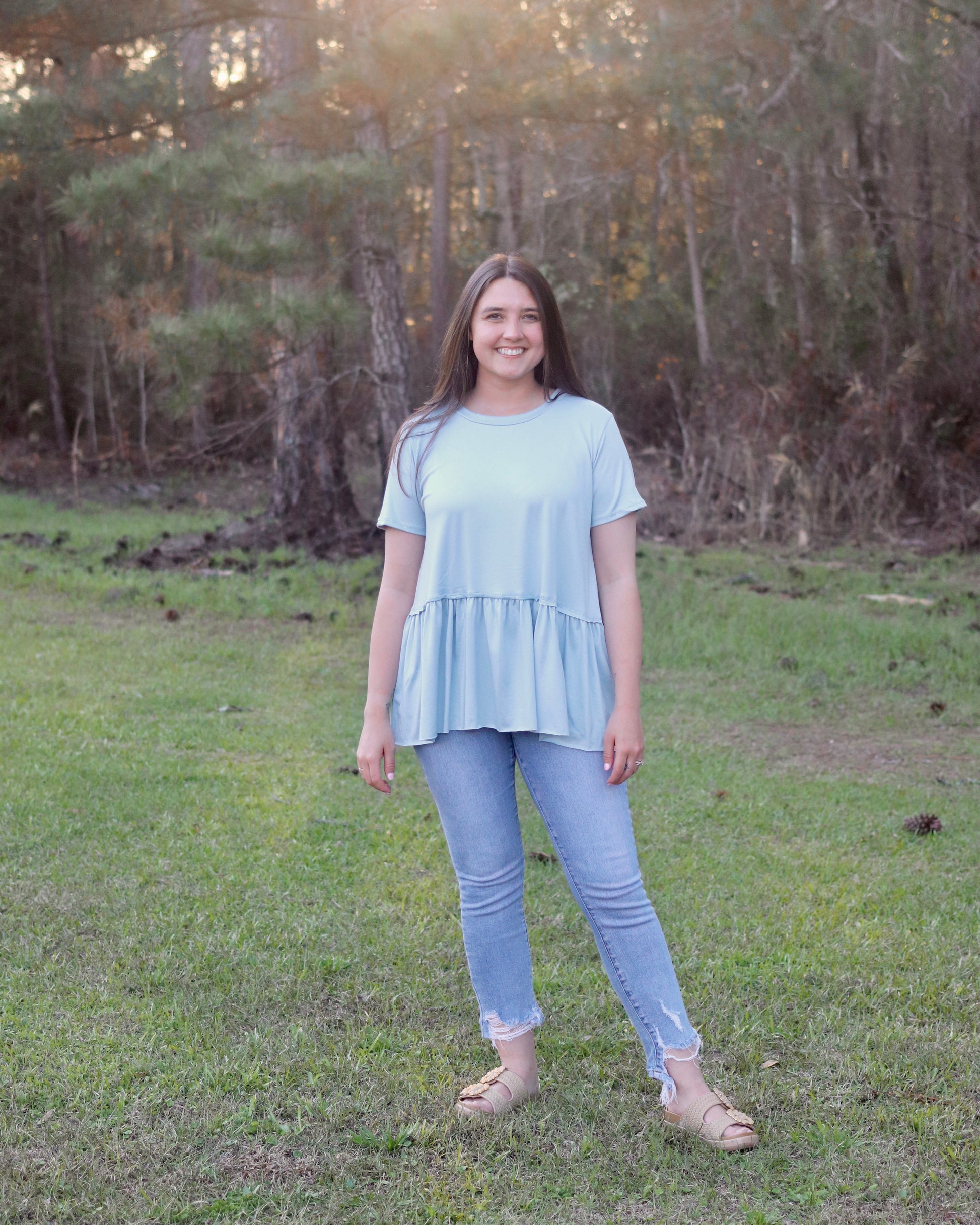 Woman standing in a grassy field with trees in the background