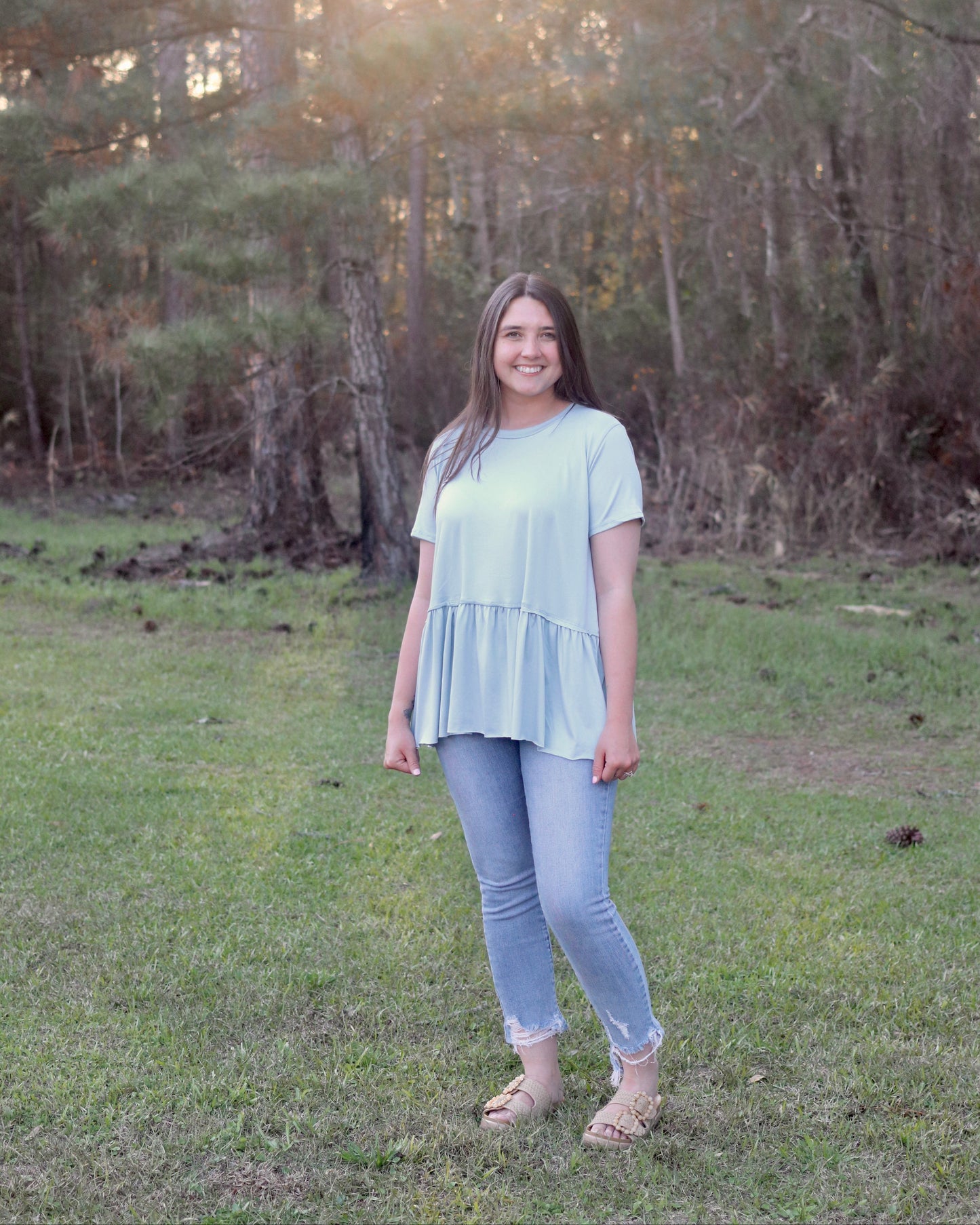 Woman standing in a grassy field with trees in the background