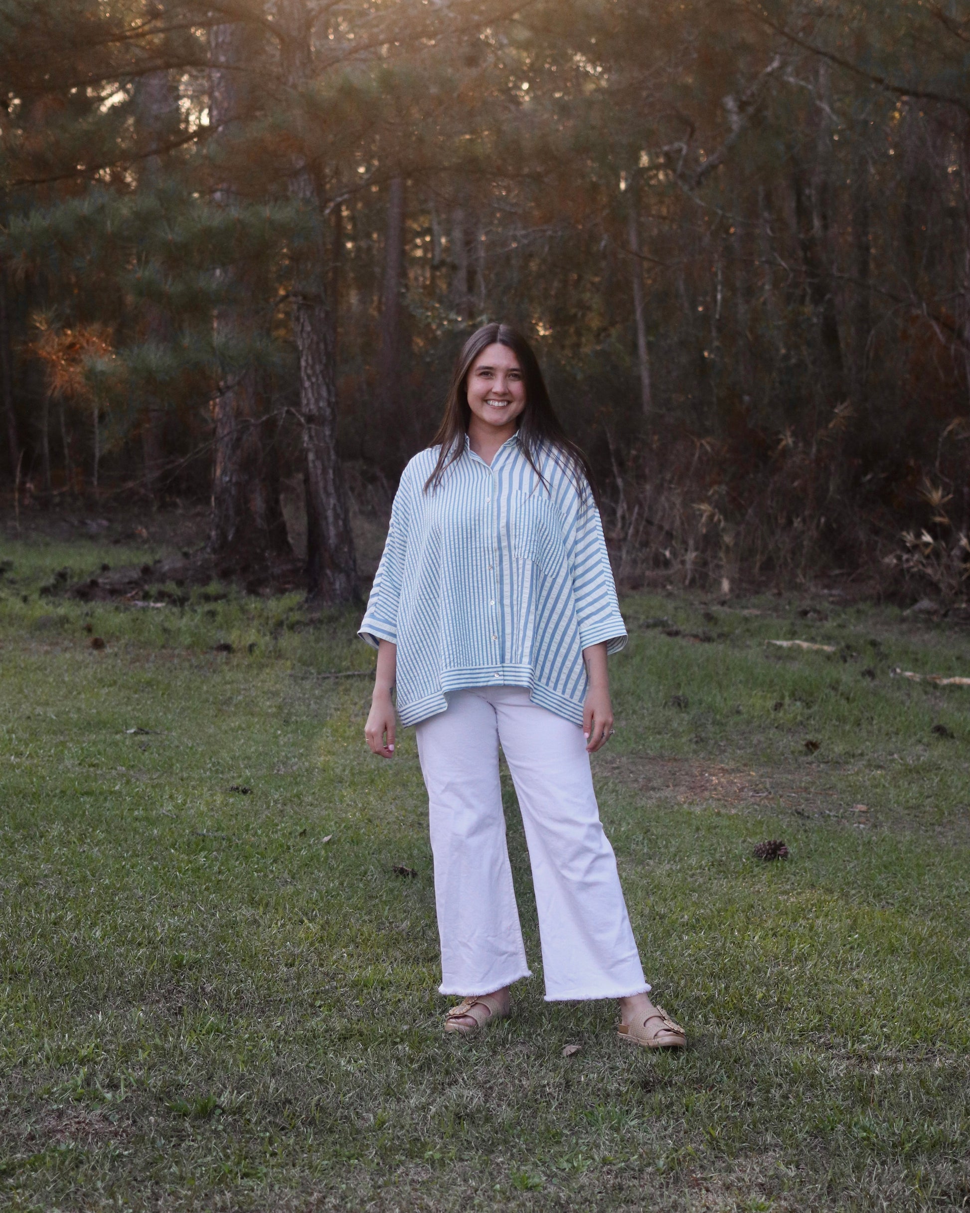 Woman standing in a grassy field with trees in the background