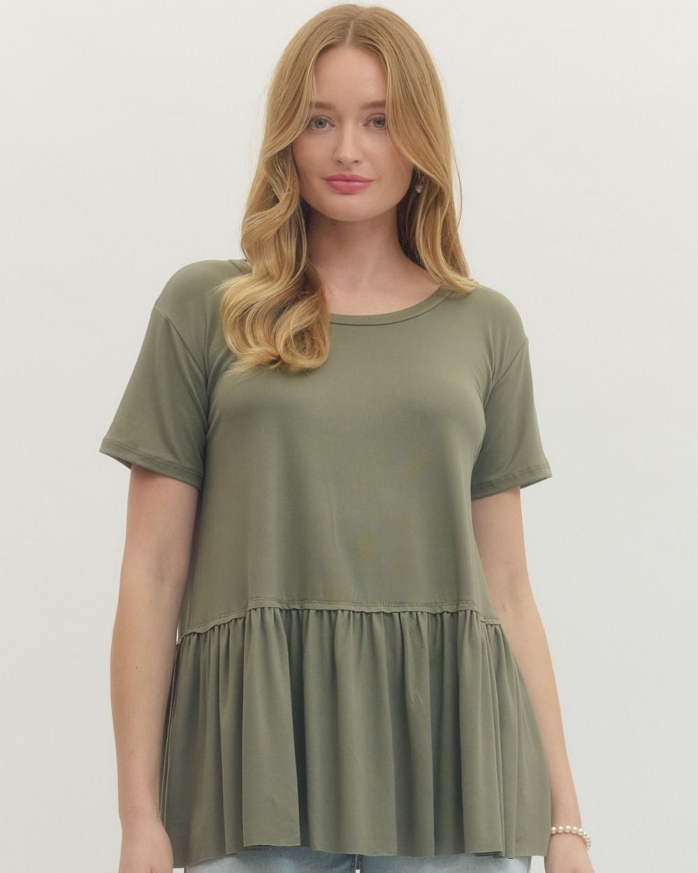 Woman wearing an olive green peplum top and light blue jeans on a white background