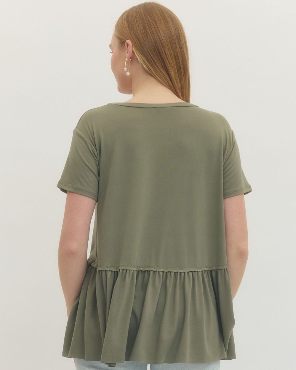 Person wearing an olive green layered tunic with light blue jeans on a white background