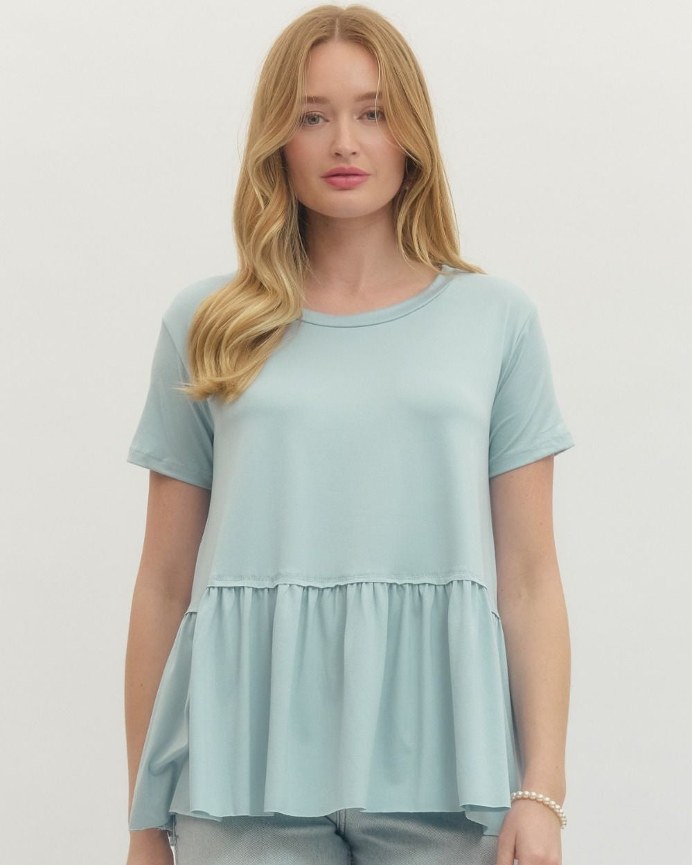 Woman wearing a light blue peplum top and pants against a neutral background